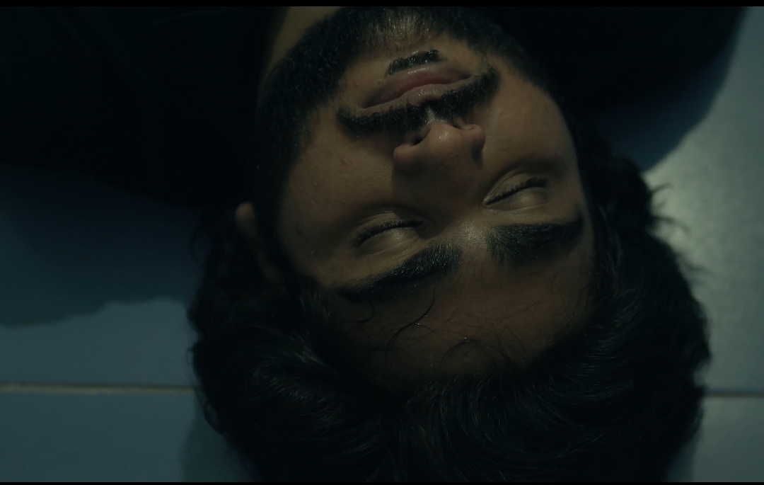 A man lying upside down in a dark frame from Qaid.
