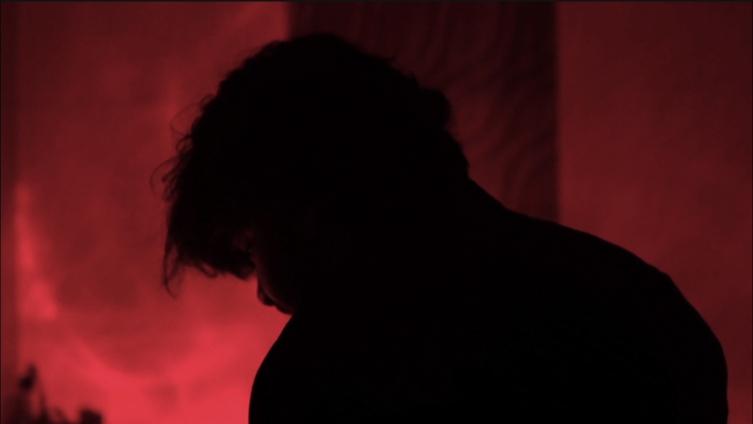 A silhouetted figure surrounded by red light in Qaid.