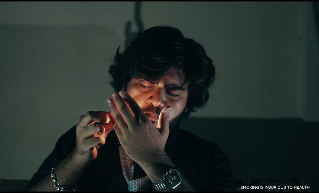 The protagonist lighting a cigarette in a dimly lit scene from Qaid.
